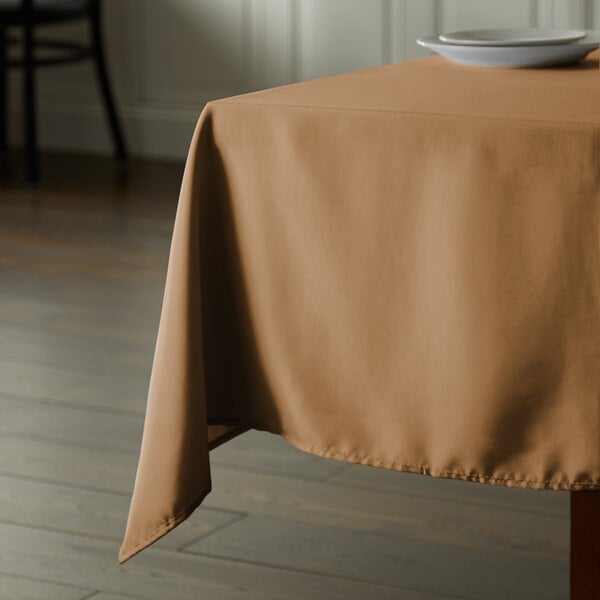 A table with a beige Intedge cloth table cover and a plate on it.