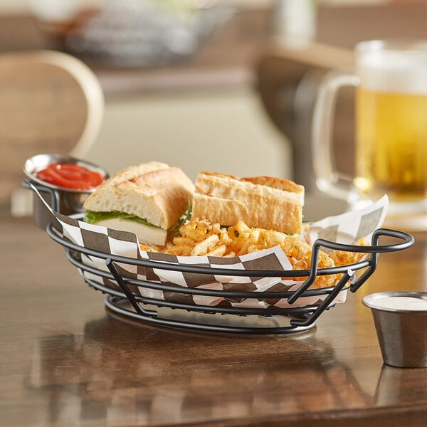 An American Metalcraft black wire basket with a sandwich and fries on a table.