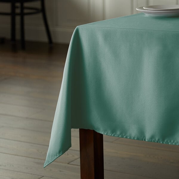 A table with a seafoam green square tablecloth on it.