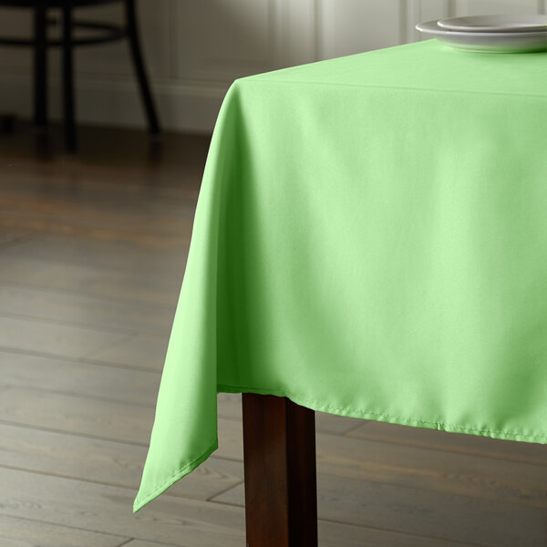 A square seafoam green polyester table cover with hemmed edges on a wooden table.