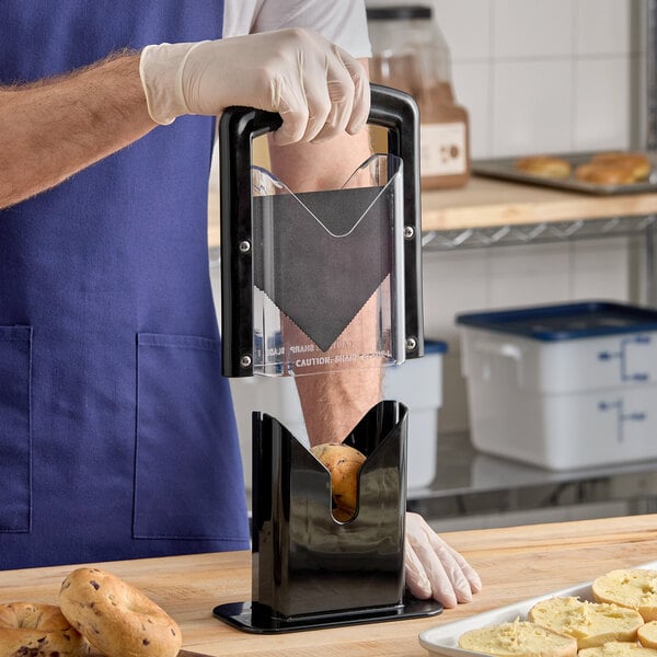 A black bagel slicer being used to cut a bagel in a kitchen setting.