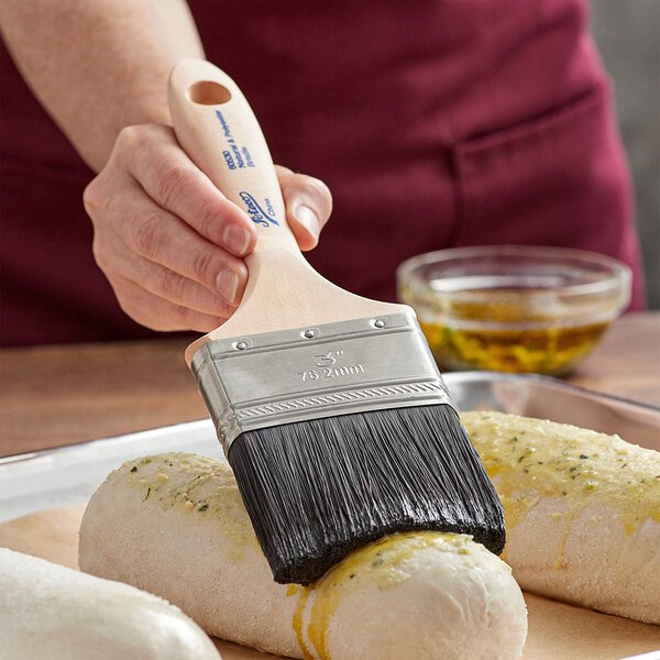 A person using an Ateco boar bristle pastry brush to paint food on a tray.