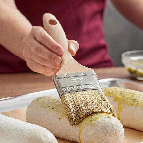 A person using an Ateco boar bristle brush to paint food on a tray.