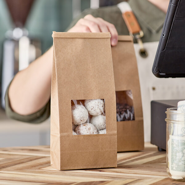 A person holding two brown Kraft customizable tin tie bags with white and brown objects in them.