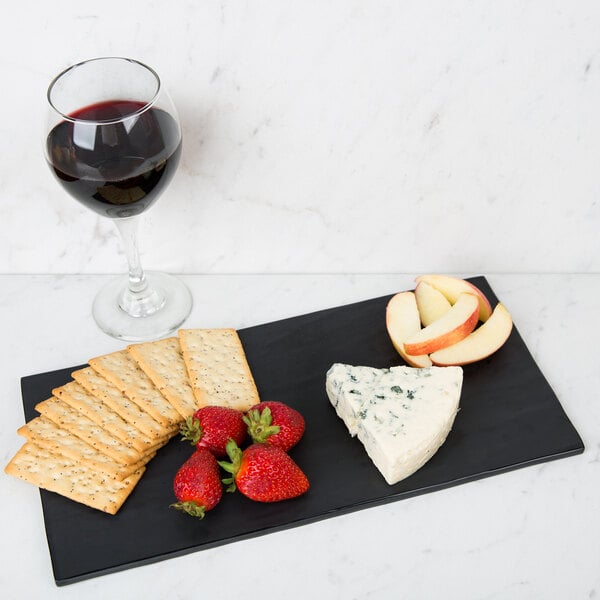 A black GET Melamine charcuterie board with cheese, fruit, and crackers with a glass of red wine.