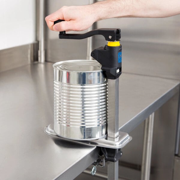 A commercial can opener with a long handle mounted on a stainless steel countertop, being used to open a large can.
