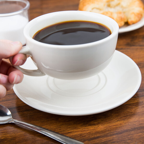 A hand holding a cup of coffee on a CAC Ivory China saucer.