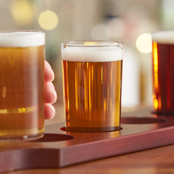 A hand holding a Libbey juice glass of beer with foam.
