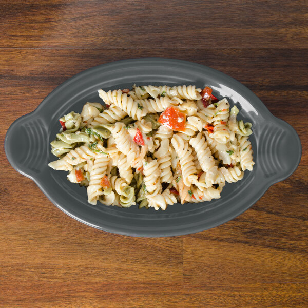 A Fiesta oval china baker filled with pasta and vegetables on a wood table.
