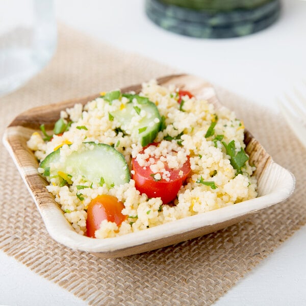 A wooden Eco-gecko palm leaf bowl filled with couscous, tomatoes, and cucumbers.