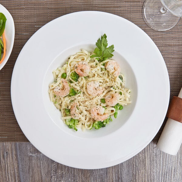An Arcoroc white porcelain pasta bowl filled with shrimp and vegetable pasta.