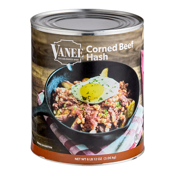 A can of Vanee Corned Beef Hash on a table with a pan of food and a spoon.