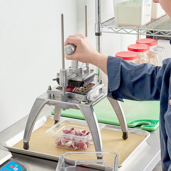 A person using a Nemco Easy Chopper III to dice vegetables into a plastic container.