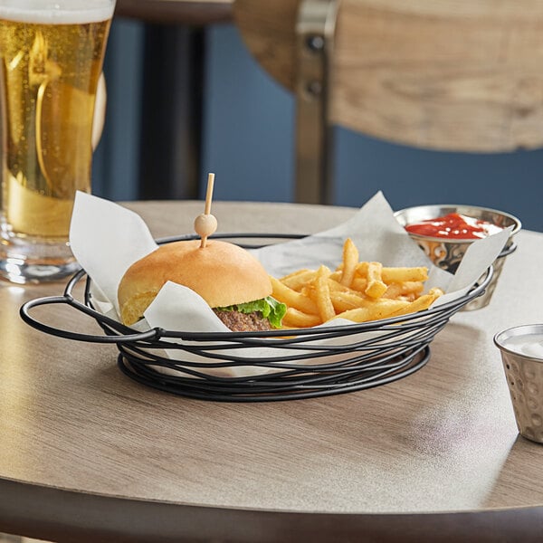 A Tablecraft black metal restaurant basket with a bowl of ketchup and french fries.
