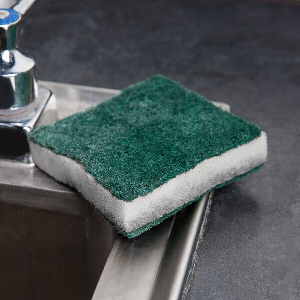 A green Scrubble by ACS tough-scour sponge on a metal surface.