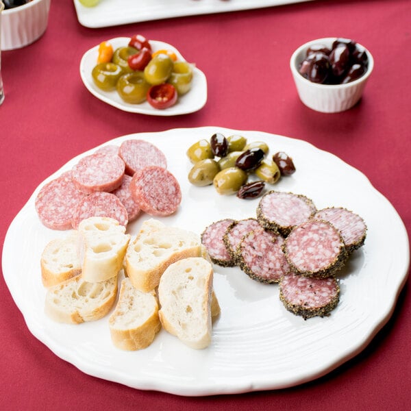 A bright white oval porcelain platter with spiral cut edges holding a plate of food on a table.