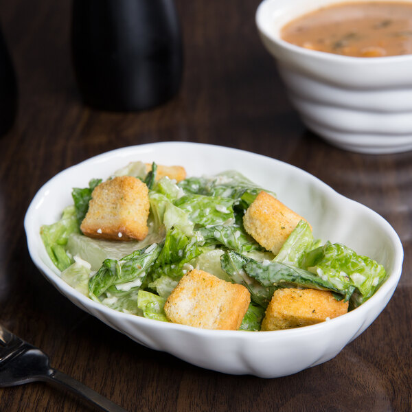A bright white porcelain large elliptical bowl filled with salad with croutons.