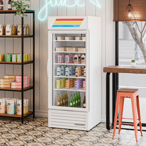 A white refrigerated glass door merchandiser with LED lighting, stocked with various beverages and food items.