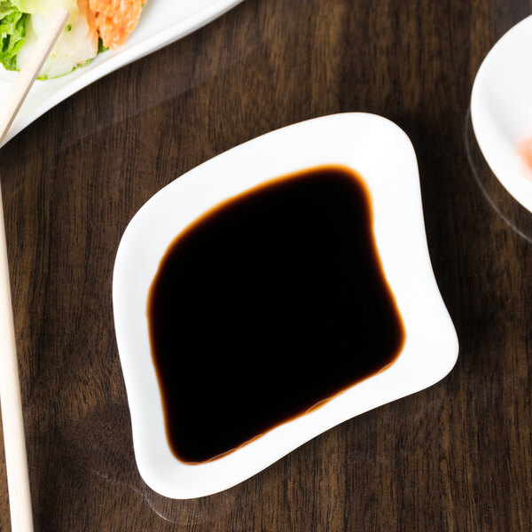 A white 10 Strawberry Street porcelain plate with sushi and a bowl of soy sauce on it.