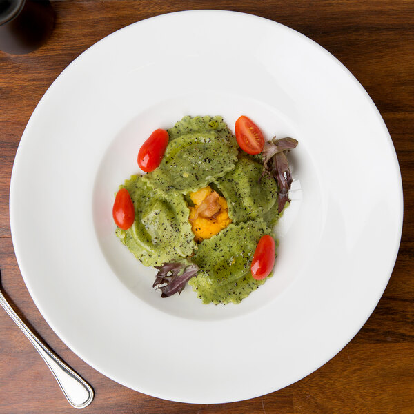 A 10 Strawberry Street white bone china pasta bowl filled with pasta, tomatoes, and vegetables on a table.