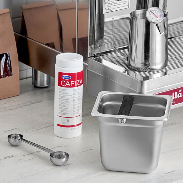 A metal container with a white and silver Urnex Cafiza container next to it.