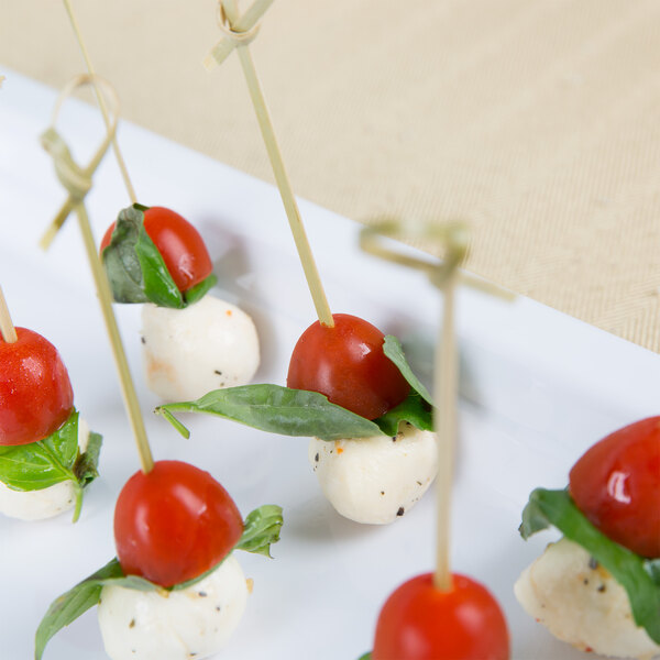 A table set with a white Thunder Group melamine food pan filled with appetizers including tomatoes and basil.