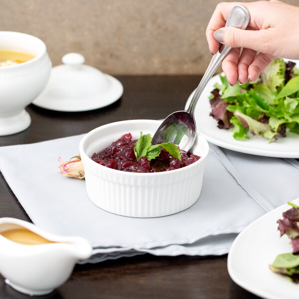 A person holding a spoon in a bowl of cranberry sauce.