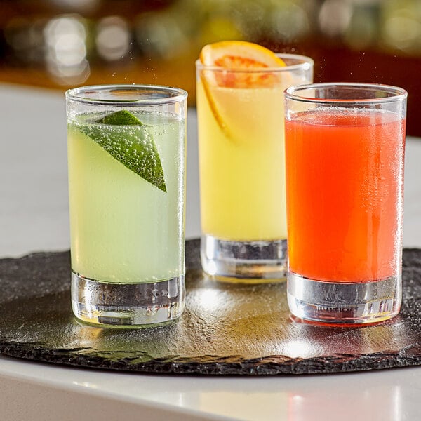 A tray of Arcoroc Islande juice glasses filled with drinks of different colors, including orange.