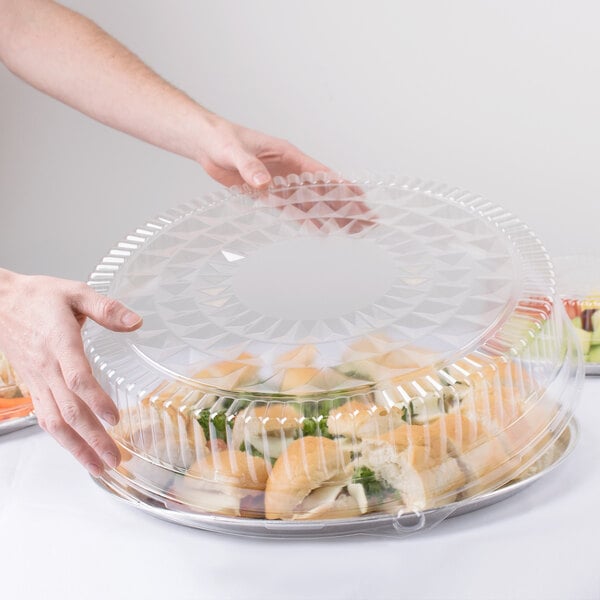 A person holding a Durable Packaging clear plastic high dome lid over a container of food.