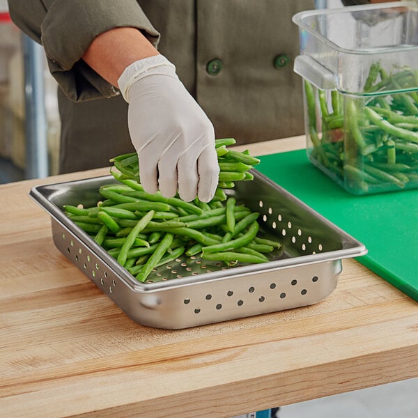 A person wearing gloves putting green beans in a Vollrath stainless steel pan.