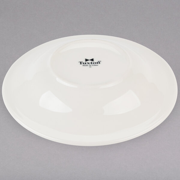 A Tuxton eggshell china soup bowl with a black logo and black text on it.