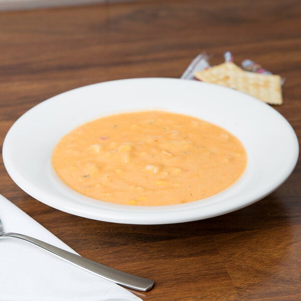 A Tuxton eggshell china soup bowl with a spoon and cracker on a table.