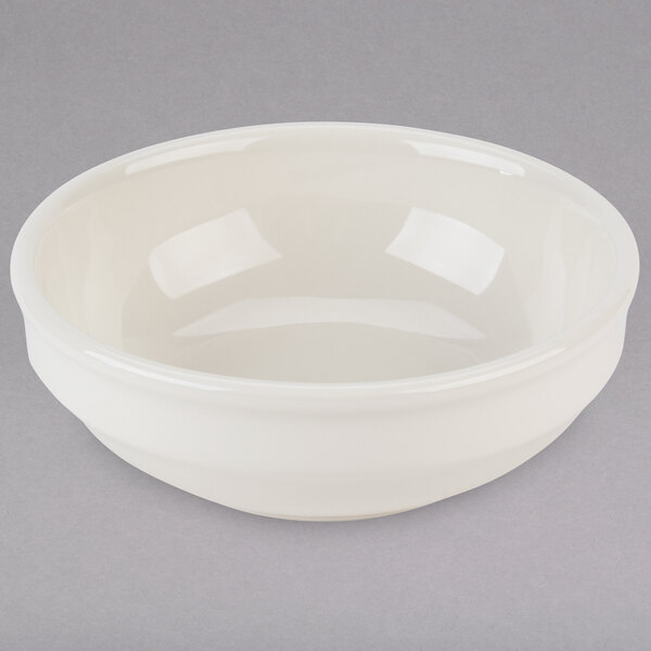 A white Tuxton China bowl with a small rim on a gray surface.