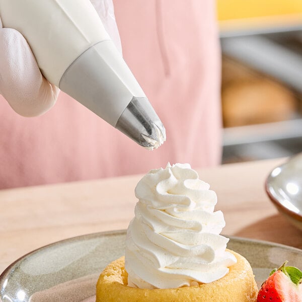 A person's hand using an Ateco closed star piping tip to pipe pastry cream onto a dessert.