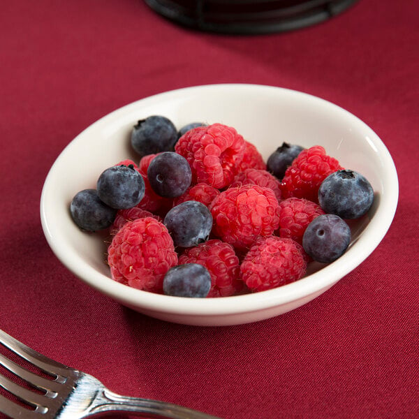 A Tuxton eggshell china bowl filled with raspberries and blueberries on a table with a fork.