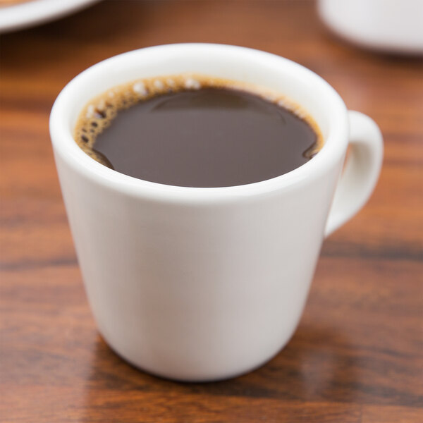 A Tuxton eggshell tall china cup filled with coffee on a table.