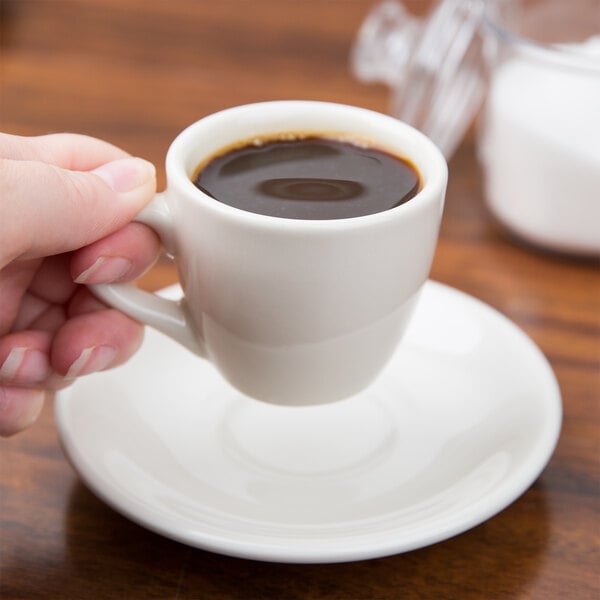 A person holding a Tuxton Reno saucer with a cup of coffee on it.