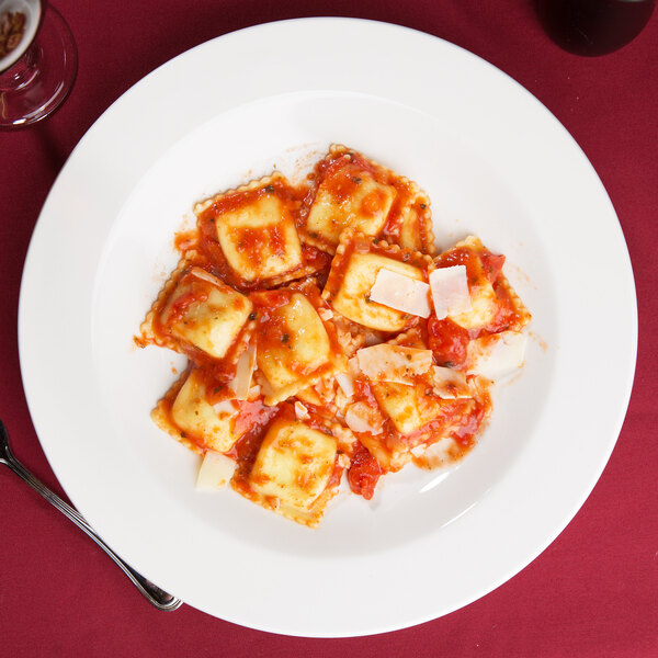 A Tuxton Nevada eggshell china pasta bowl filled with ravioli in sauce and cheese with a fork.