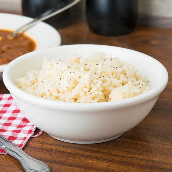 A Tuxton eggshell china bowl filled with rice and soup with a spoon in the soup.