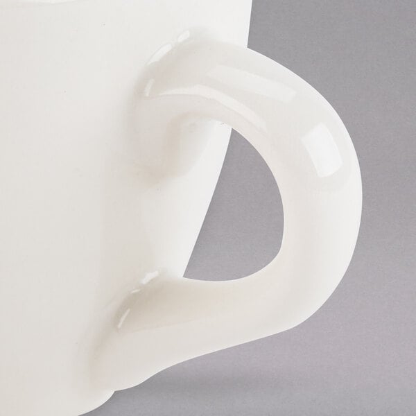 A close up of a Tuxton eggshell white espresso cup with a handle.