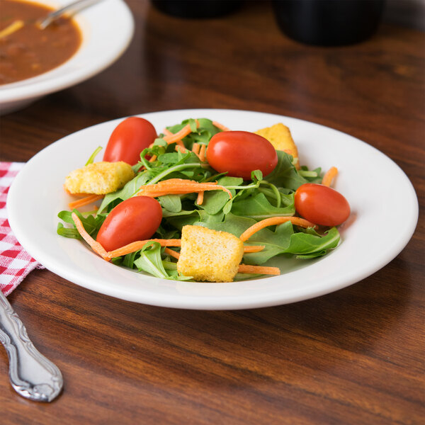 A Tuxton Reno eggshell wide rim china plate with a salad with tomatoes, carrots and other vegetables.