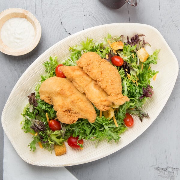 An oval EcoChoice palm leaf tray with fried chicken and salad on it.