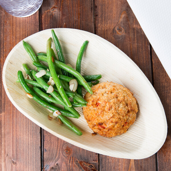 A TreeVive by EcoChoice oval palm leaf tray with green beans and a biscuit on a wooden table.
