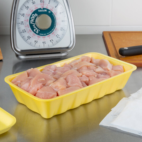 A yellow CKF foam meat tray with raw chicken on a scale.