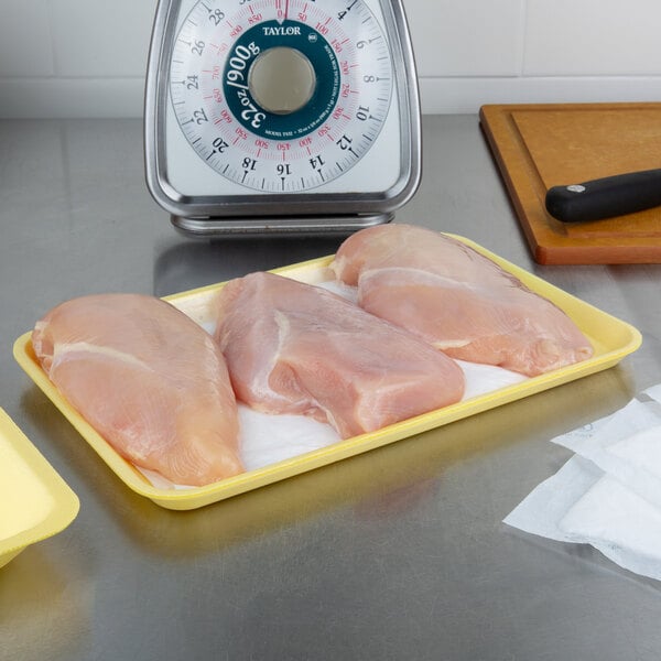 A yellow CKF foam tray holding two raw chicken breasts on a counter.