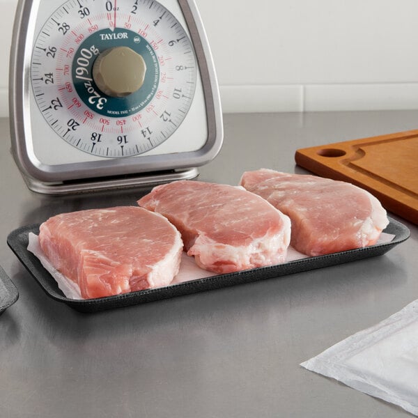 A black CKF foam meat tray holding raw meat on a counter.