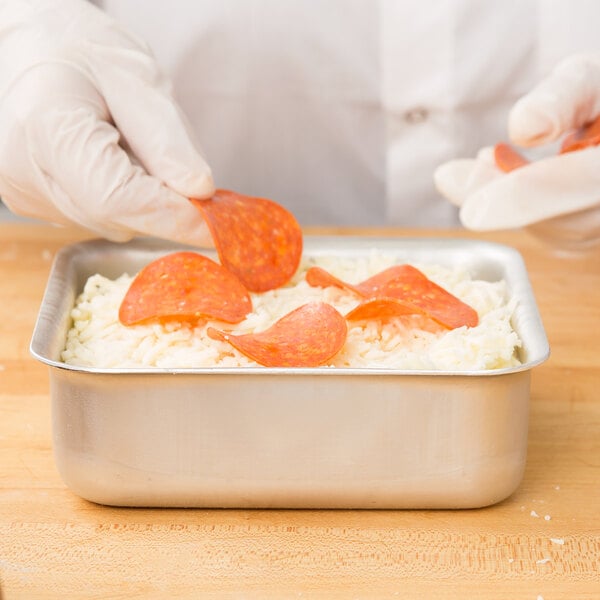 A person using an American Metalcraft aluminum pizza pan to prepare a pizza.