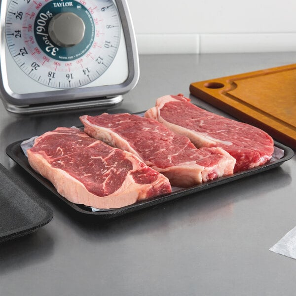 A black CKF foam meat tray holding raw meat on a counter.