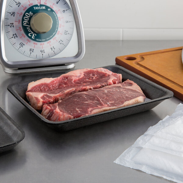 A black CKF foam meat tray holding raw steaks on a counter.