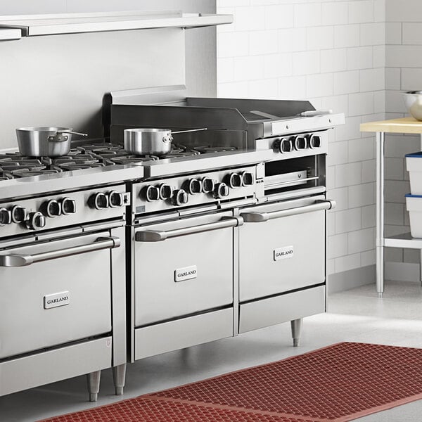 A large commercial stainless steel range with six burners, a raised griddle/broiler, and two standard ovens.